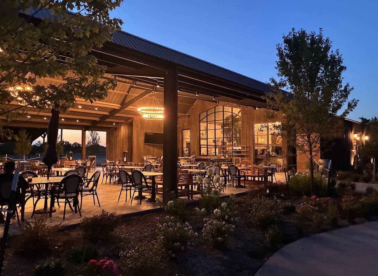 Covered outdoor dining and landscaped beds at dusk